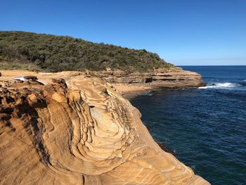 Scenic view of rocks in sea against clear blue sky