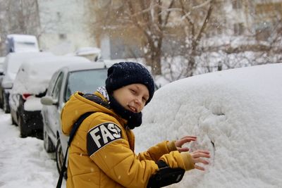 Portrait of boy by snow on car during winter