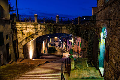 Arch bridge over canal amidst buildings against sky at night