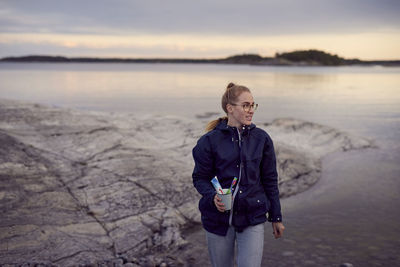 Young woman walking with toothbrush and toothpaste in container at beach during sunset