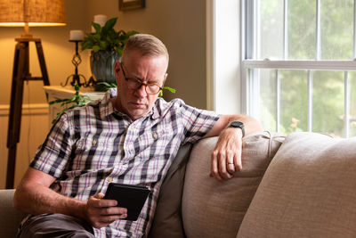 Midsection of man using mobile phone while sitting on sofa at home