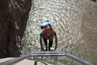 Portrait of female backpacker climbing ladder on sunny day