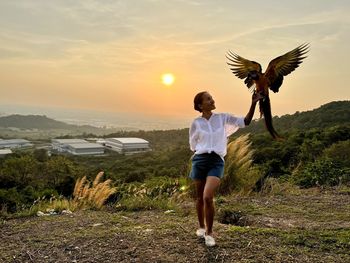 Rear view of woman standing on field against sky during sunset