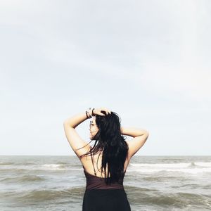 Young woman standing by sea against sky