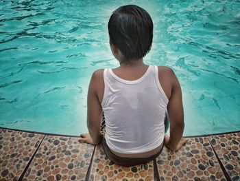 Rear view of boy sitting on swimming pool