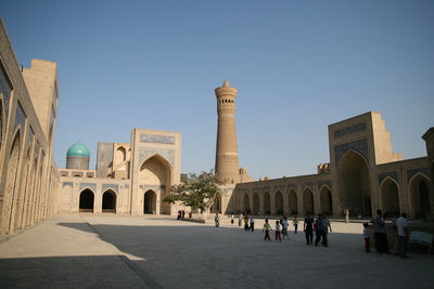 People visiting po-i-kalyan and kalyan minaret against clear blue sky