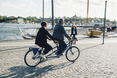 Full length of senior couple riding tandem bike on road in city during vacation