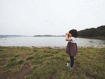 Full length of young girl standing on shore and looking against sky