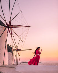 Rear view of woman standing by windmill against sky during sunset