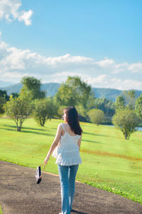 Rear view of woman walking on field against sky