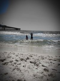 Silhouette people on beach against clear sky