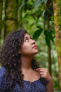 Woman with curly hair looking up while standing by tree