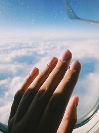 Close-up of hand against sky seen through window