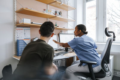 Female medical expert explaining reports to teenage boy on computer while sitting in doctor's office