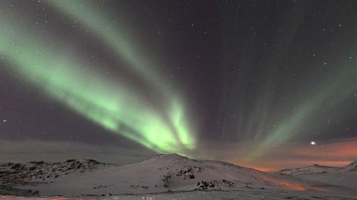 Scenic view of aurora borealis over mountains during winter