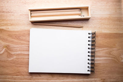 High angle view of note pad and pencils on wooden table