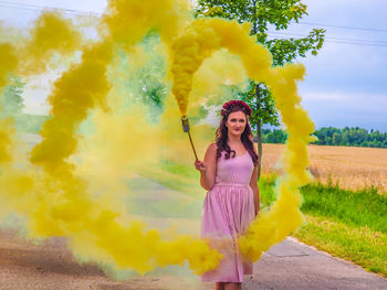 Portrait of young woman holding distress flare while standing on footpath