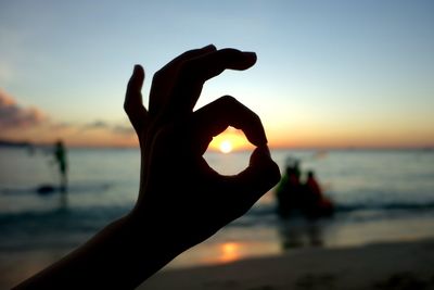 Optical illusion of silhouette hand holding sun against sea during sunset