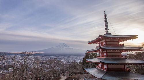 View of temple by building against cloudy sky