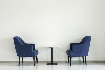 Empty chairs on table against white wall