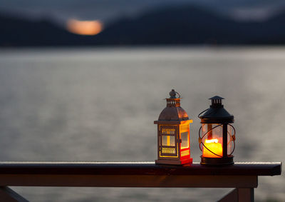 Illuminated lamp on table by sea against sky during sunset