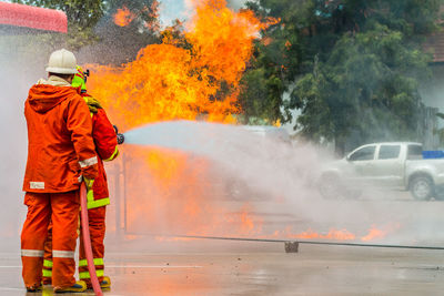 Rear view of firefighter spraying water on fire while standing at street