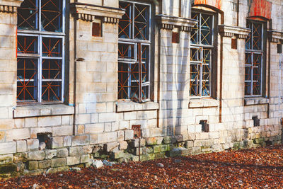 Close-up of an old stone building with damaged walls, barred windows, fallen leaves covering ground