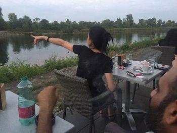 Rear view of woman sitting on table at lake