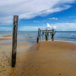 Wooden posts on beach against sky