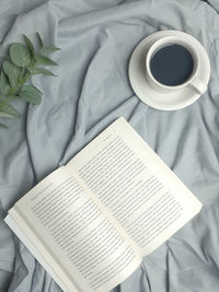 High angle view of coffee cup with book on bed