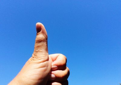 Cropped image of hand showing thumbs up against clear blue sky