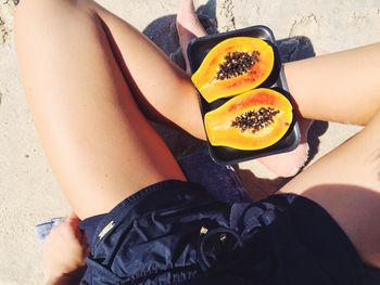 Low section of woman holding fruits on beach