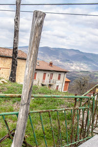 Fence by tree and buildings against sky