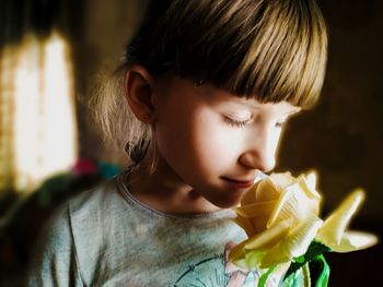 Close-up of girl smelling yellow rose at home