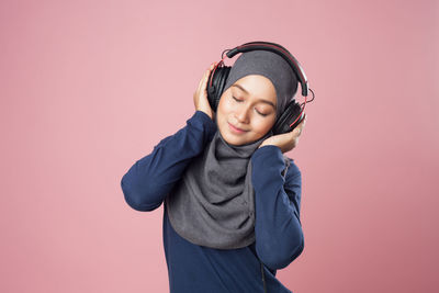 Young woman listening music against pink background