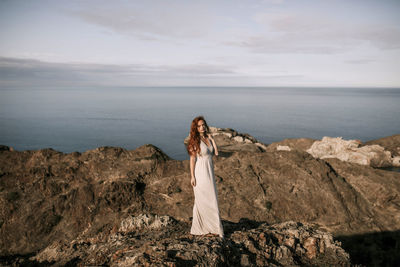 Woman standing on rock by sea against sky