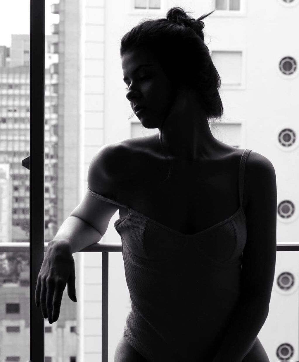 WOMAN LOOKING AWAY WHILE STANDING AGAINST WINDOW