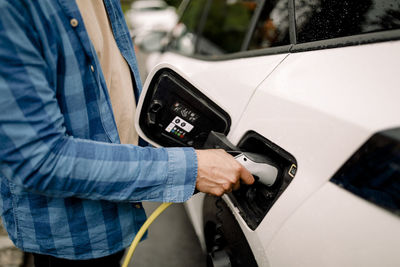 Midsection of man plugging charger in electric car