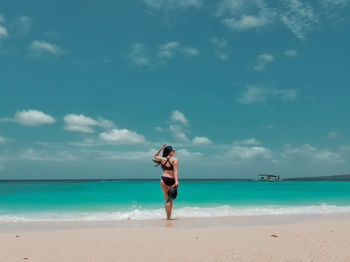 Rear view of bikini woman standing on beach against cloudy sky