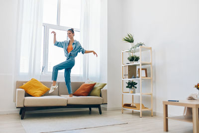 Full length of woman using digital tablet while sitting on sofa at home