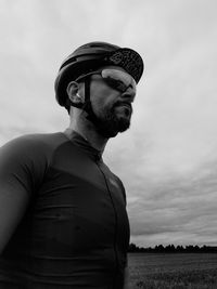 Low angle view of man wearing cycling helmet on field against cloudy sky