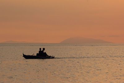 Silhouette people sitting on boat in sea against orange sky during sunset