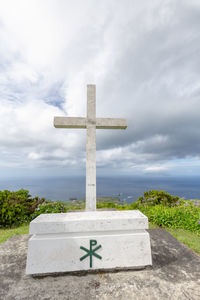 Cross sign on land against sky