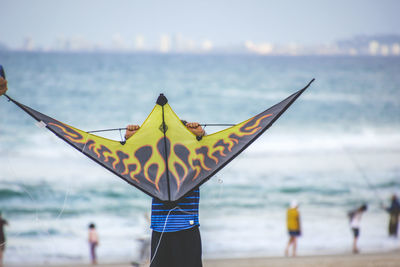 Boy holding kite while standing at beach