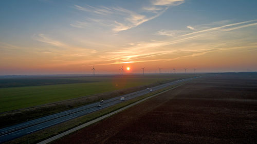 Road amidst field against sky during sunset