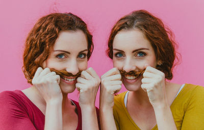 Portrait of smiling siblings making mustache with hair against pink background