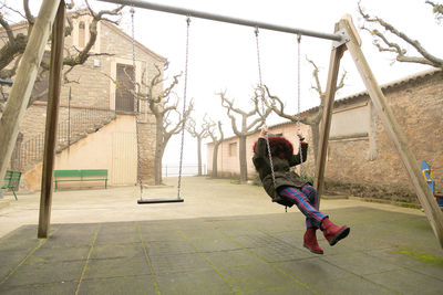 Young girl sheltered in an abandoned swing set with hood, unrecognisable.