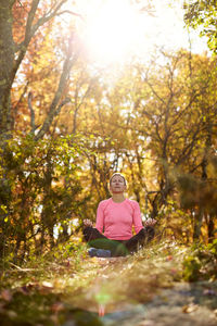 Woman sitting on street amidst trees during autumn