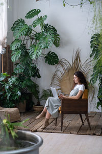 Female freelance botany expert working online in urban jungle interior or home garden