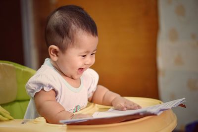 Close-up of cheerful baby girl with book on high chair